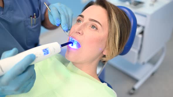 Dentist Doctor Using Dental Curing Light Equipment for Filling, Examining a Patient's Teeth in