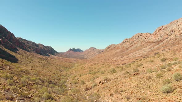 Aerial drone shot past hikers viewing arid valley, Central Australia