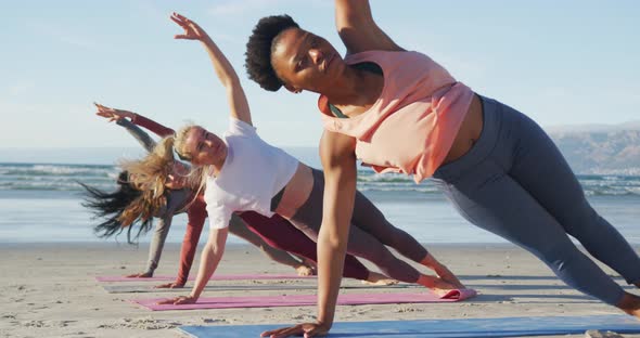 Group of diverse female friends practicing yoga at the beach