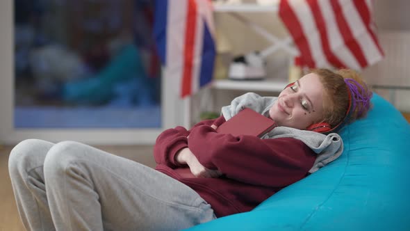 Satisfied Young Caucasian Woman Hugging Laptop Yawning and Falling Asleep on Bag Chair at Home