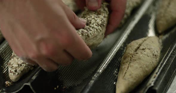 Baker Taking Dough On Baguette Tray After Proofing And Dipping It On Multi Grains Inside The Bakery.