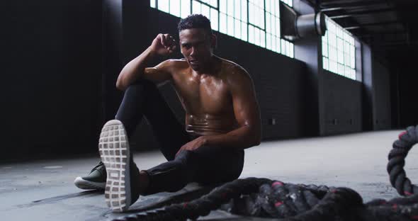 Shirtless african american man resting after battling ropes in an empty urban building