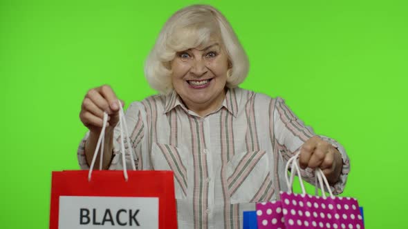 Elderly Grandmother in Shirt Showing Black Friday Inscription on Shopping Bags, Rejoicing Discounts