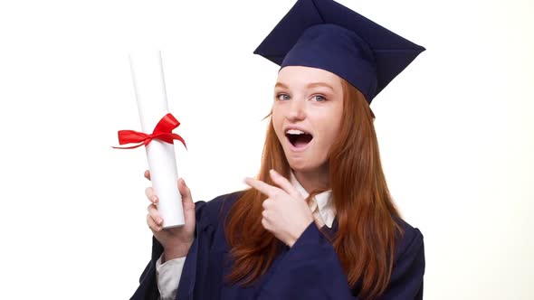 Exciting Caucasian Ginger Graduate Girl in Blue Robe and Square Academical Cap Showing Diploma