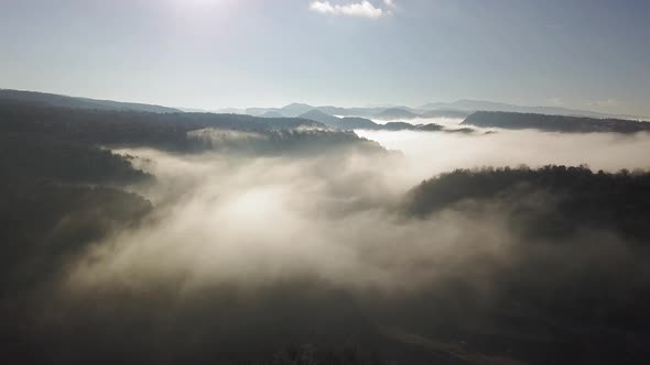 Flying over forested mountains, clouds covering the peaks. Pantà de Sau, Tavertet.