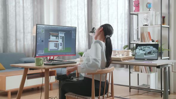 Asian Woman Engineer Stretching While Designing House On A Desktop At Home