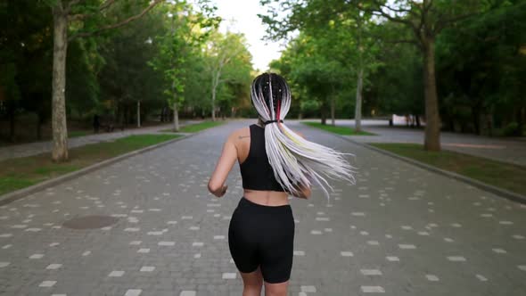 Slow Motion Rear View of European Woman with Black and White Dreadlocks Running By Local Green Park