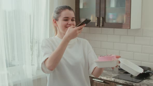 A Woman Takes a Picture on a Smartphone of a Cake in a Gift Box