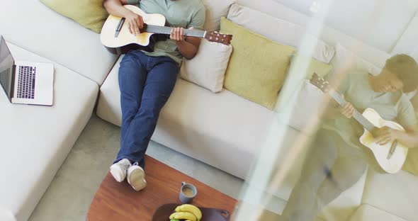 African american man plays guitar and singing, using laptop at home