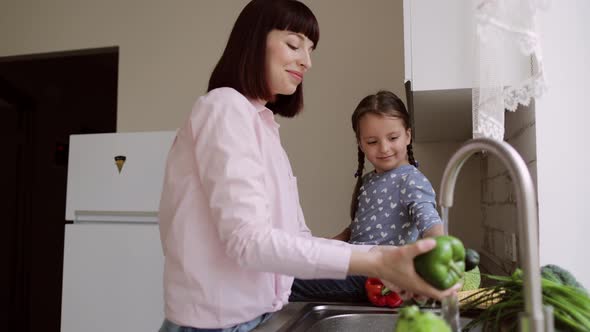 Young Beautiful Mother and Her Cute Daughter Washing Vegetables Peppers Cucumbers and Tomatoes