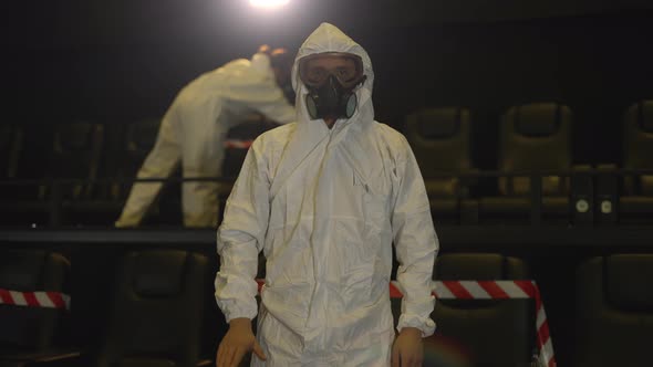 A Man Showing Stop Sign  Standing in the Empty Cinema Wearing White Protection Costume