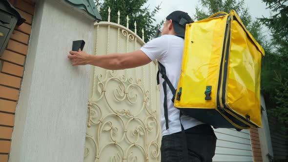 Bottom Angle View of Confident Courier Ringing Door Bell on Gate Standing Outdoors on Summer Day