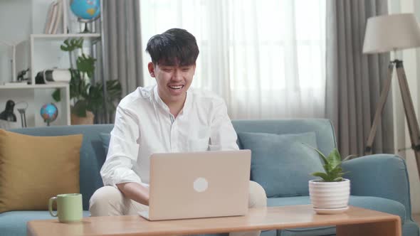 Smiling Asian Man Having Video Call On Laptop Computer While Sitting On Sofa In The Living Room
