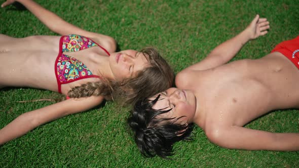 Top View of Cute Romantic Couple of Little Kids Lying on Green Summer Grass Warming in Sunshine