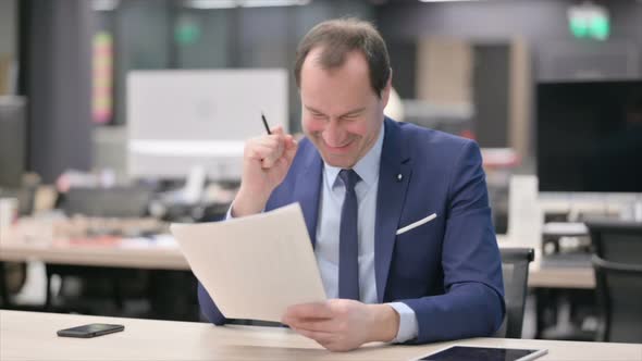 Businessman Celebrating Success While Reading Documents in Office