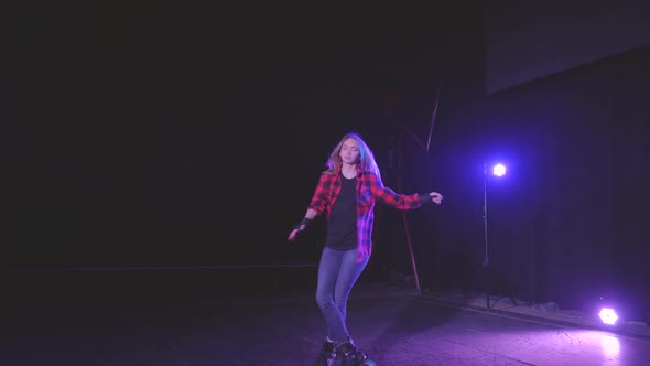 Active Young Attractive Girl on Roller Skates Professionally Spinning on Front Wheels in Dark Scene