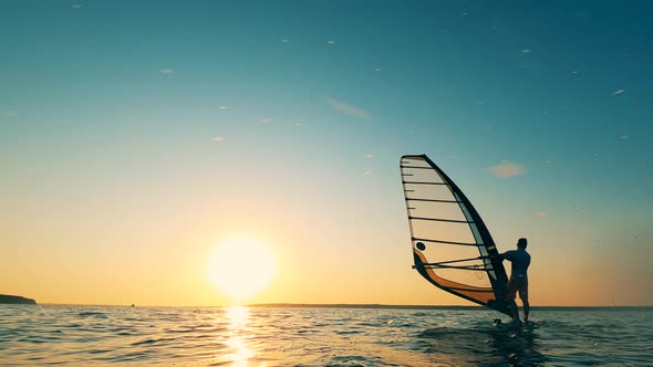 A Man Is Sailboarding Along the Shore at Sunset