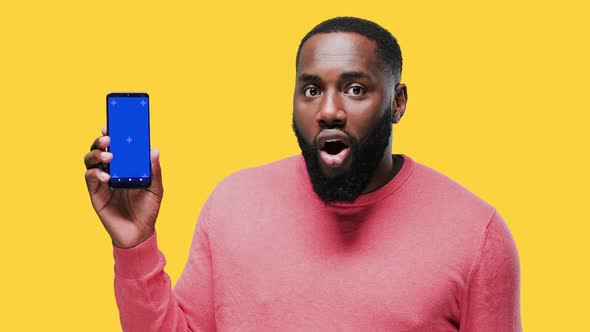 Happy Young Black Guy Showing His Phone Screen with Chroma Key and Pointing To It on Yellow