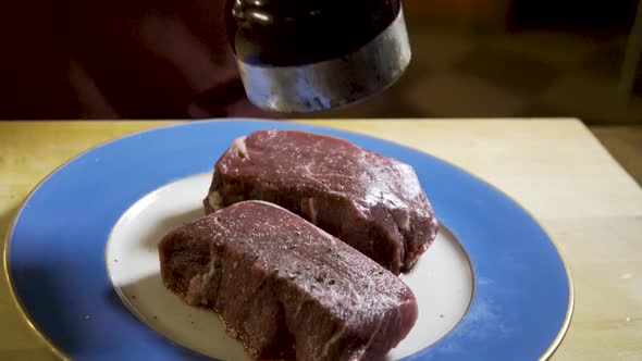 As camera slides from right to left, a chef grinds fresh black pepper onto two large pieces of raw,