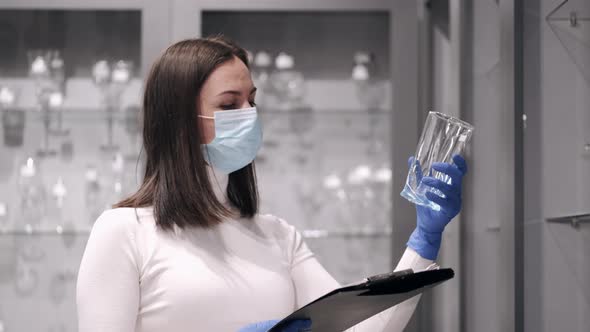 The Serious Woman in Mask Is Checking the Glassware in a Shop