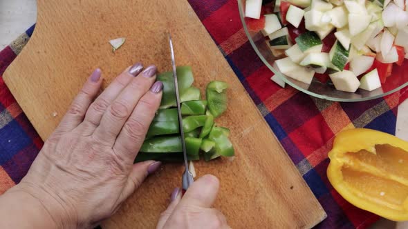 Top down view of woman's hands using a santoku knife and slicing green sweet pepper on a wooden cutt