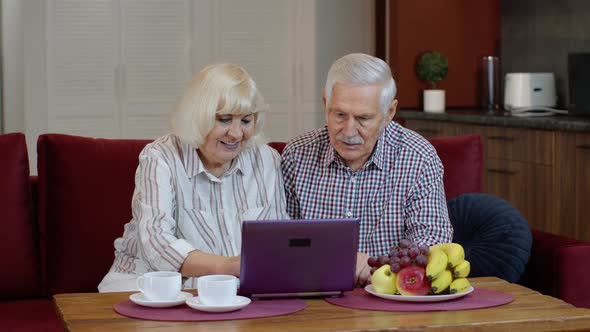 Senior Old Couple Grandparents Talking and Using Digital Laptop Computer at Home. Internet Shopping