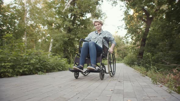 Caucasian disabled person woman sitting wheelchair on sidewalk in park, front view.