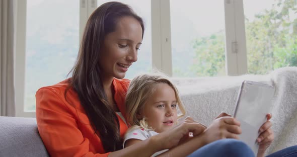 Mother and daughter using digital tablet on sofa at home 4k