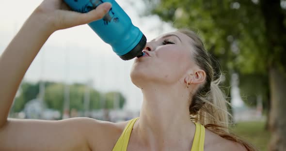 Fitness Woman Drinking Water From Bottle After Running Exercise in City Park. Portrait of Sport Girl