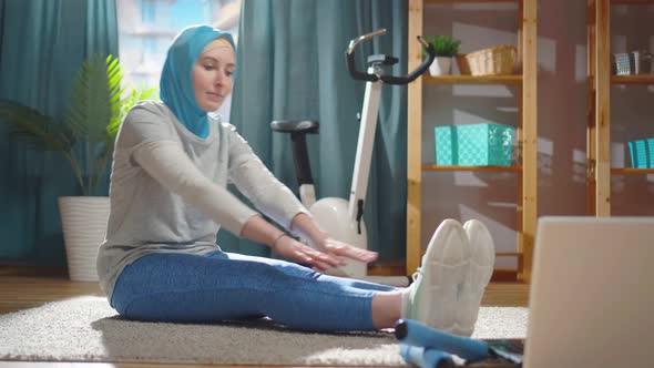 Beautiful Young Muslim Woman in a National Headscarf is Warming Up in Front of a Laptop