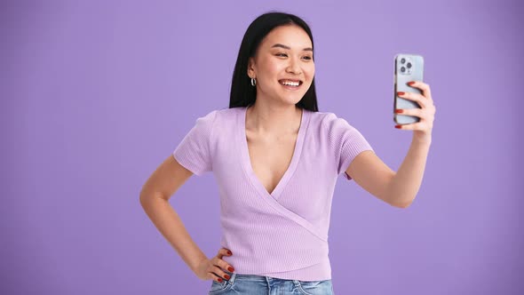 Smiling Asian brunette woman wearing purple t-shirt talking by video call on mobile