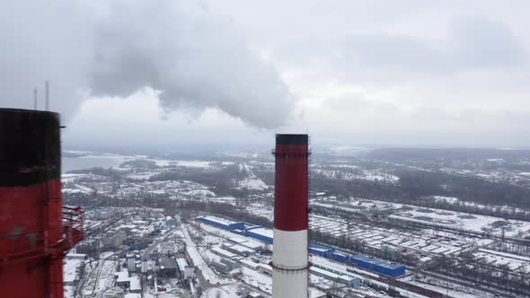 Aerial View of Two Big Red and White Factory Pipes Rising Over the Snowy Industrial Cityscape alt