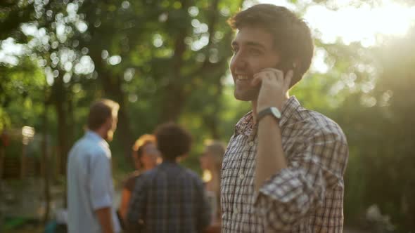 Young Attractive Male with Light Bristle and Plaid Shirt Talking on Mobile Phone in Park While