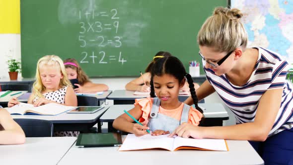 Teacher helping schoolgirl with their homework in classroom