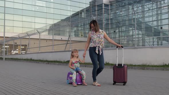 Mother, Daughter Walking From Airport After Vacation. Woman Carrying Luggage. Child Rides Suitcase