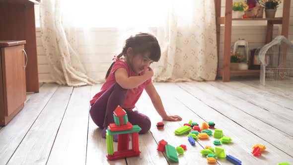 Little Beautiful Girl Sits on the Floor in the Room and Plays with a Colorful Constructor