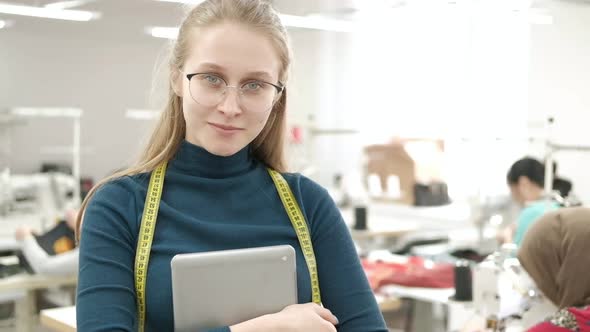 dressmaker in clothing factory among working seamstresses with tablet in hands