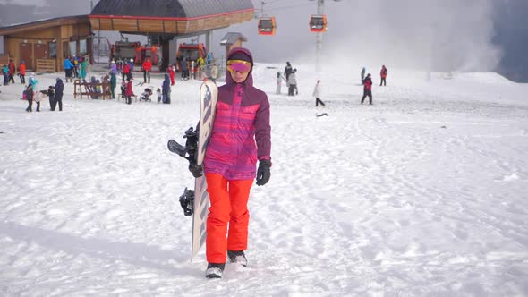 Girl Snowboarder Holding Snowboard in Hands at the Ski Resort, Sport Woman in Snowy Mountains, Sunny