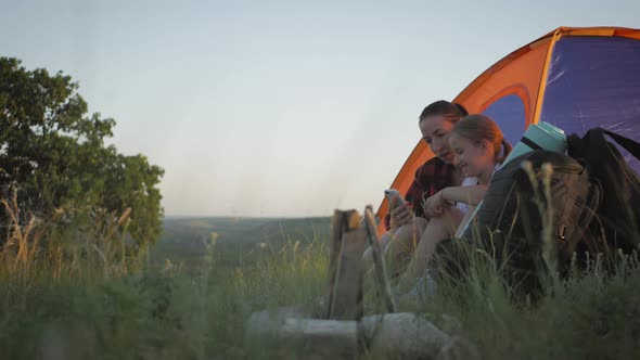 Girl with Phone While Sitting Inside Tent with Her Mother. Mother and Daughter Resting in a Tent