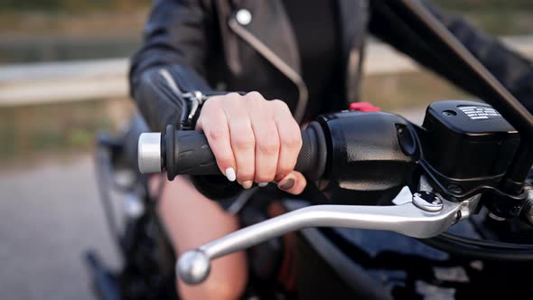 Closeup of Female Hand Twists Accelerometer Lever on Classic Black Retrostyled Motorcycle While