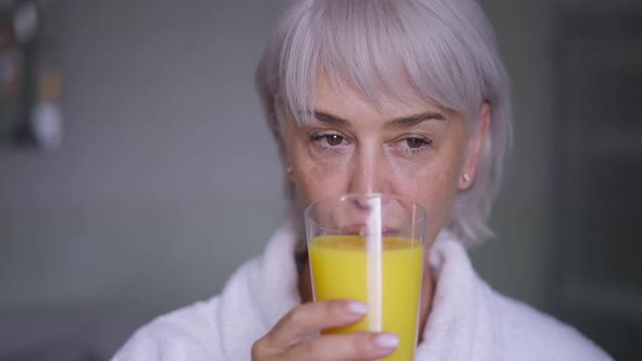 Front View Portrait Confident Middle Aged Woman Drinking Orange Juice in Slow Motion Looking Away