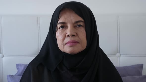 Sad Asian senior Muslim woman looking at camera, turning the face to the side