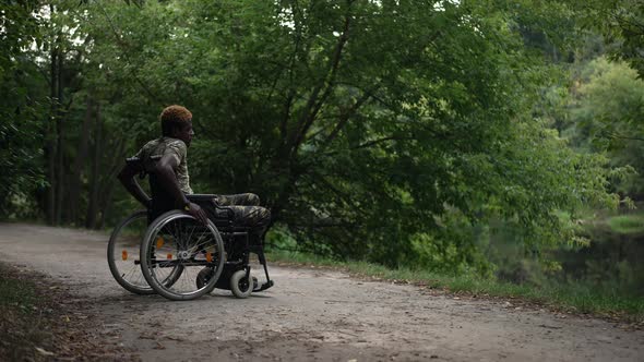 Wide Shot African American Soldier in Wheelchair Rolling to Lake Shore in Green Summer Park