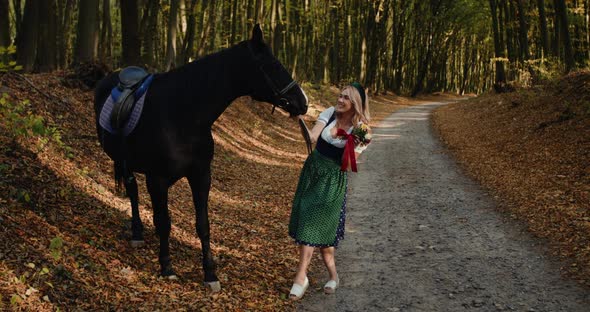Beautiful Blonde with a Bouquet of Wild Flowers Poses with Horse in Forest