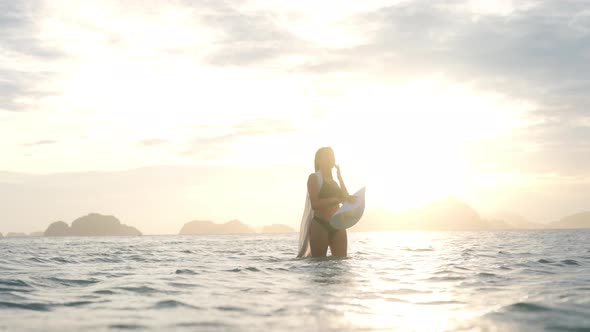 Woman In Bikini And Sun Hat Standing In Sea At Sunset