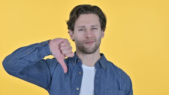 Thumbs Down By Disappointed Young Man on Yellow Background