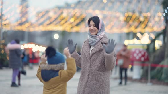 Happy Young Middle Eastern Mother Jumping with Little Son Outdoors Having Fun on Christmas Eve