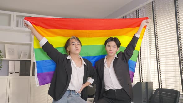 Portrait of Asian businessman gay working in office, holding LGBT flag and looking at camera.