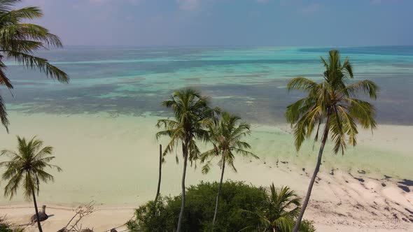 Flight of a drone over the Maldivian coast on which there are a lot of green trees, towards the ocea