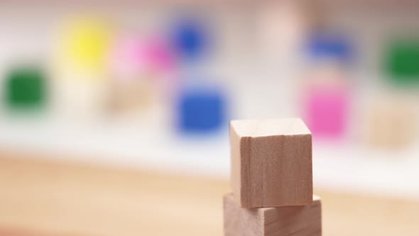 Creating a block toy tower with wooden cubes. The hand sets the top of the tower in slow motion